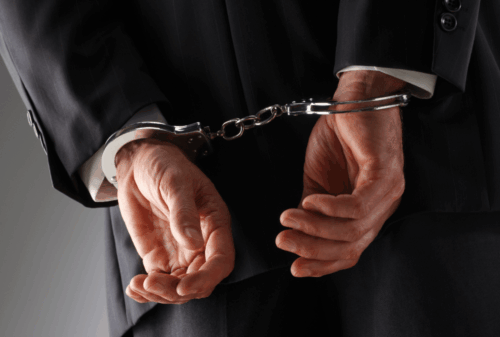Image is of a businessman in a suit with hands cuffed behind his back, concept of Cocoa Beach embezzlement lawyer
