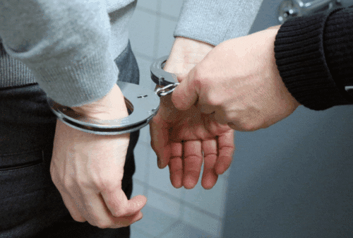 Image is of a closeup of a man's hands being put into handcuffs by a police officer, concept of Melbourne criminal defense lawyer
