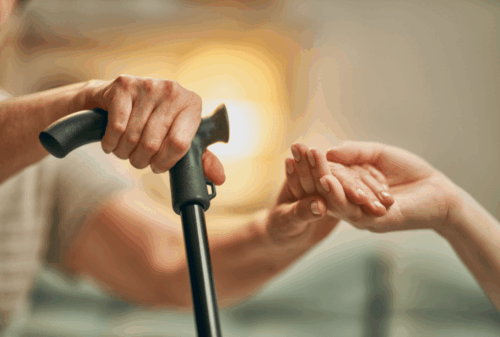 Image is of a closeup of an elder's hand on their cane and the other hand being helped by another person's hand, concept of Melbourne nursing home abuse & neglect lawyer
