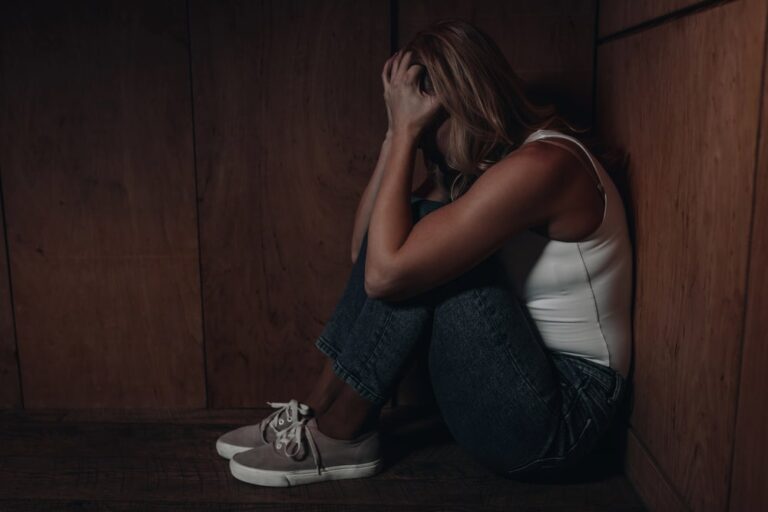 Image shows a distressed woman sitting against a wooden wall, representing emotional impact and need for protection under Florida’s laws on domestic violence