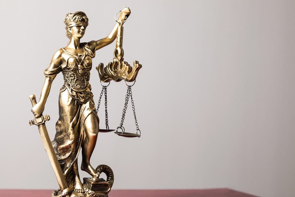 Image is of a Lady Justice statue holding scales and a sword, representing fairness and legal consequences connected to a domestic violence conviction.