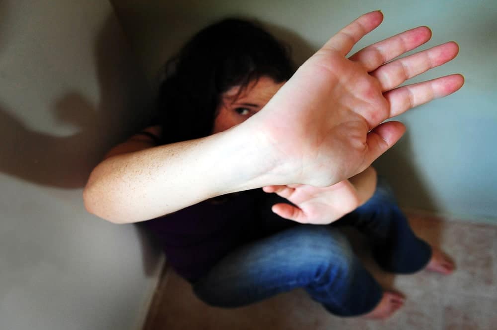 Image is of a woman sitting on the floor covering her face with her hand, concept of reporting abuse and the impact domestic violence has on legal and immigration cases.