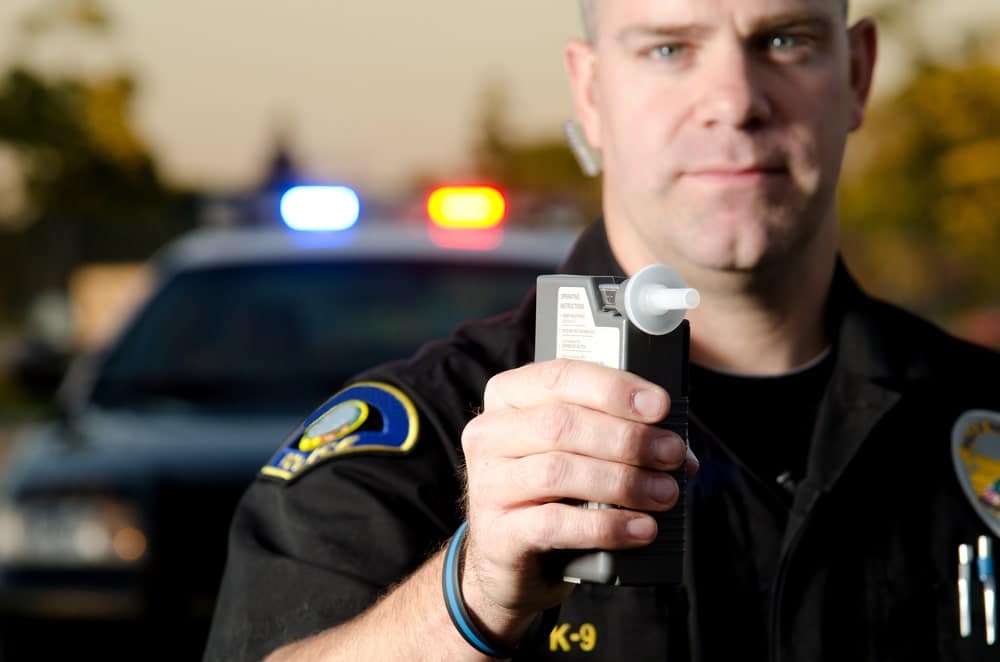 Image shows a police officer presenting a breathalyzer device, representing how DUI convictions from another state can affect a driver during a Florida traffic stop.