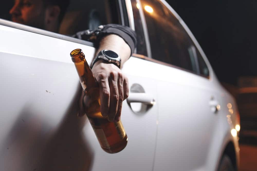 Image shows a person holding a beer bottle outside a car window, representing the risk of underage impaired driving and DUI in Florida.