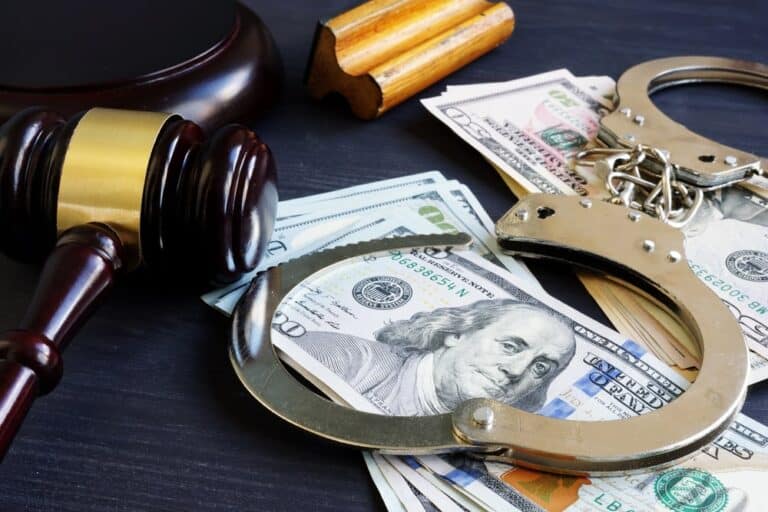 Image is of a judge’s gavel placed beside cash and handcuffs, symbolizing legal authority and financial considerations tied to a domestic violence bond.