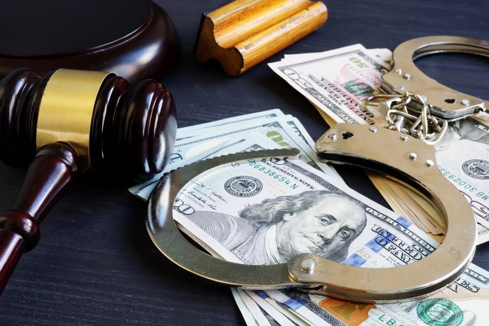 Image is of a judge’s gavel placed beside cash and handcuffs, symbolizing legal authority and financial considerations tied to a domestic violence bond.