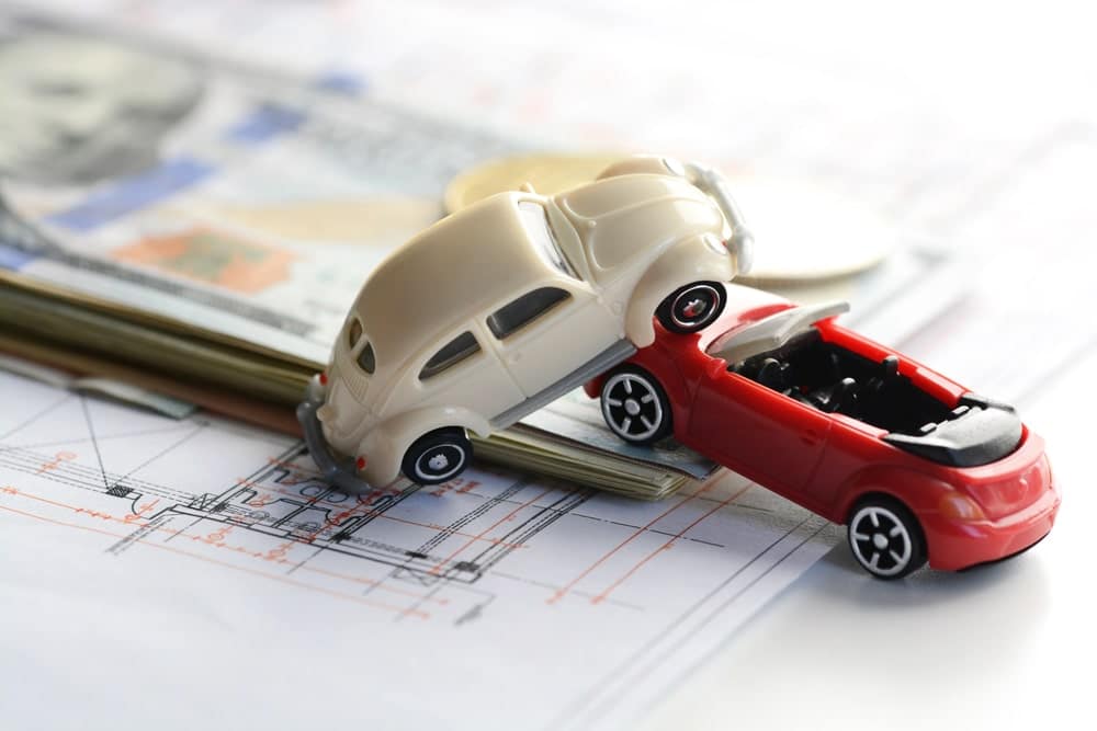 Image is of two toy cars in a crash position on top of paperwork, representing how accident claims can worsen the effect of a DUI on a driver’s insurance costs.