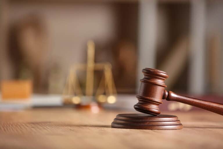 Image is of a judge gavel on a desk with justice scales in the background, concept of domestic violence arrest legal process.