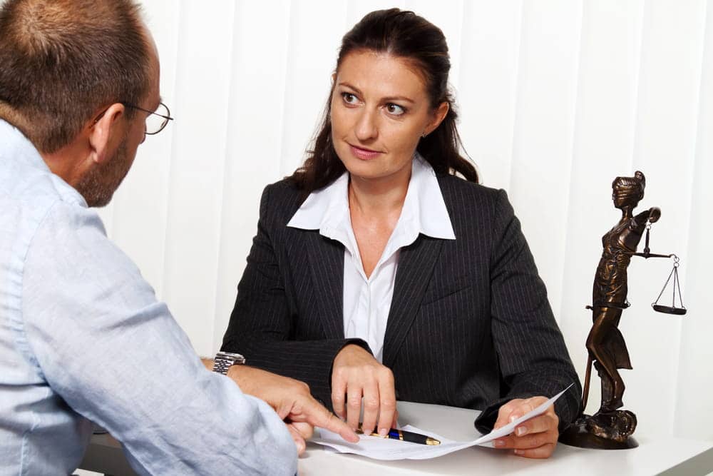 Image is of a lawyer reviewing documents with a client at a desk, concept of domestic violence arrest legal consultation.