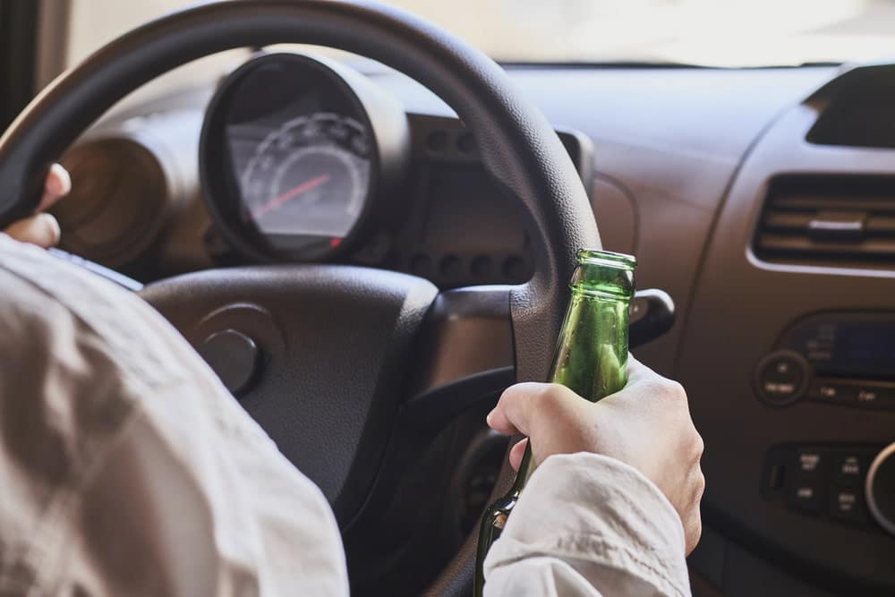 Image is of a driver holding a bottle inside a vehicle, illustrating impaired driving behavior that can permanently impact a driving record in Florida