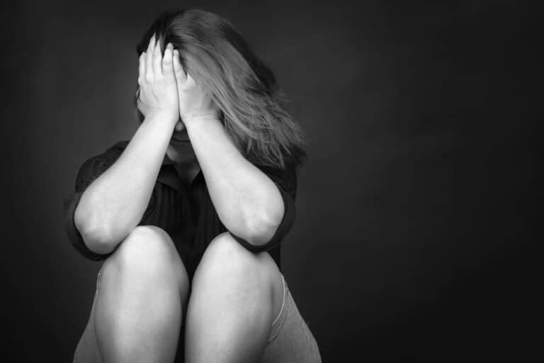 Image is of a distressed individual sitting alone with hands covering face, representing emotional impact in Florida domestic violence cases involving repeat offender allegations.