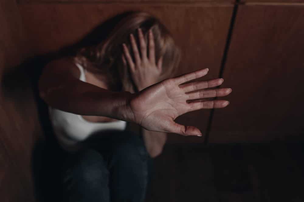 Image is of a person raising a hand in fear to protect themselves, symbolizing victim safety concerns in Florida domestic violence repeat offender situations.
