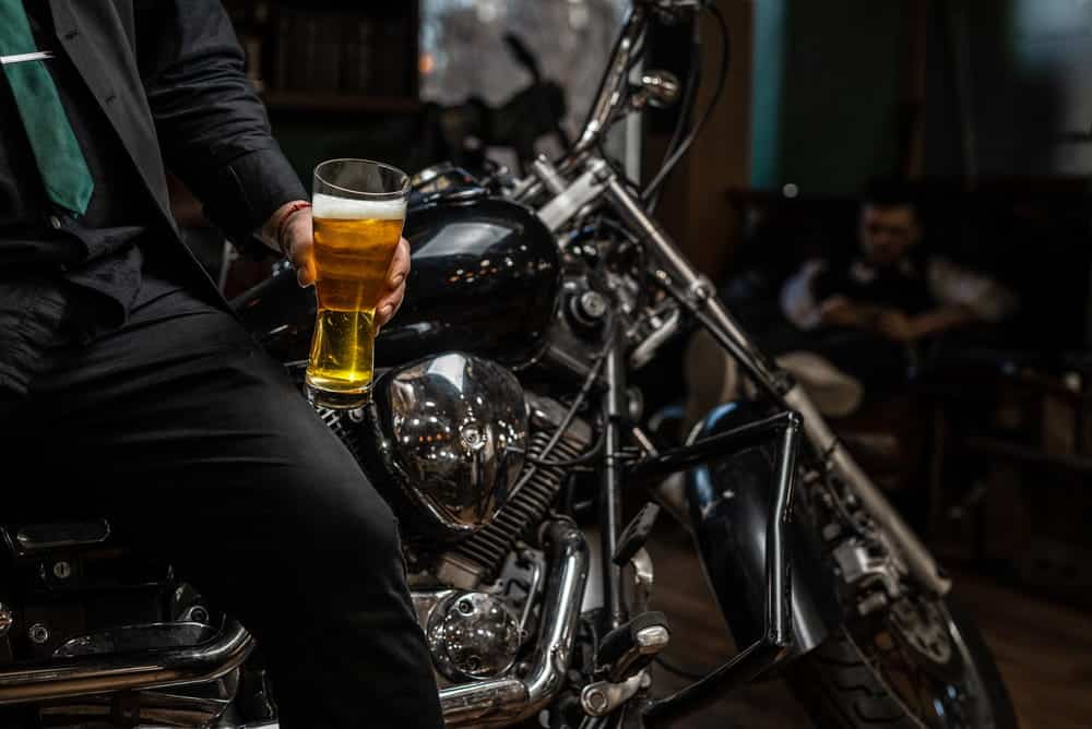 Image is of a motorcyclist holding a beer while seated on a motorcycle, showing behavior linked to DUI on a motorcycle