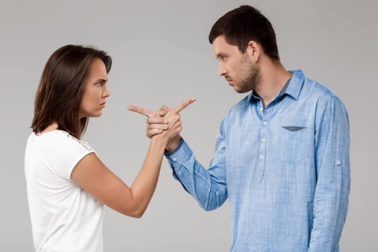 Image is of a couple confronting each other with tense gestures, concept of defending against allegations of verbal domestic violence without physical injury.