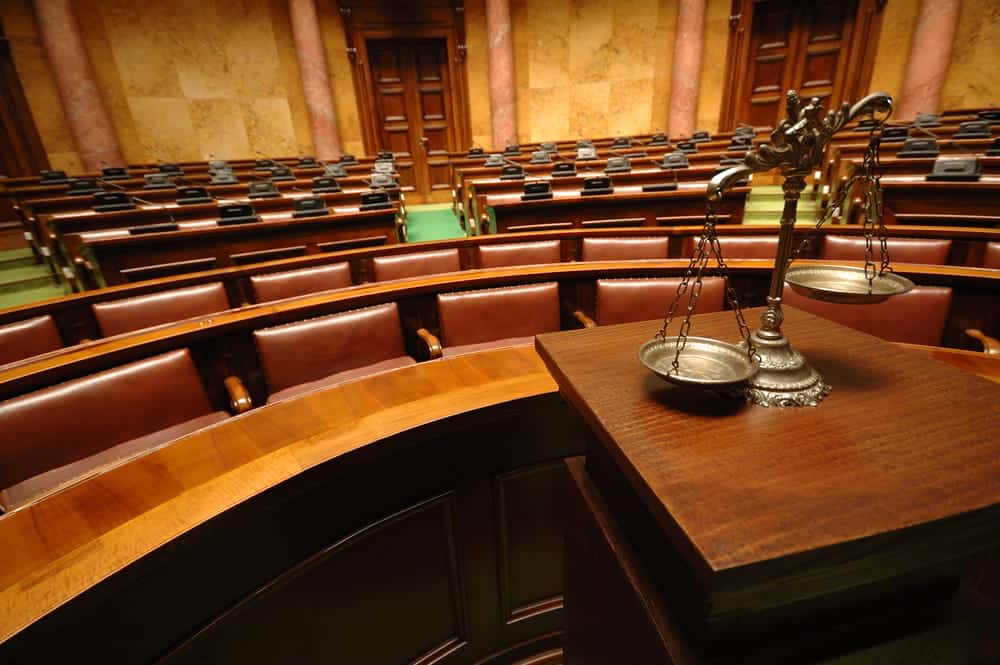 Image is of a courtroom with scales of justice in the foreground, concept of multiple DUIs in Florida and escalating legal penalties.