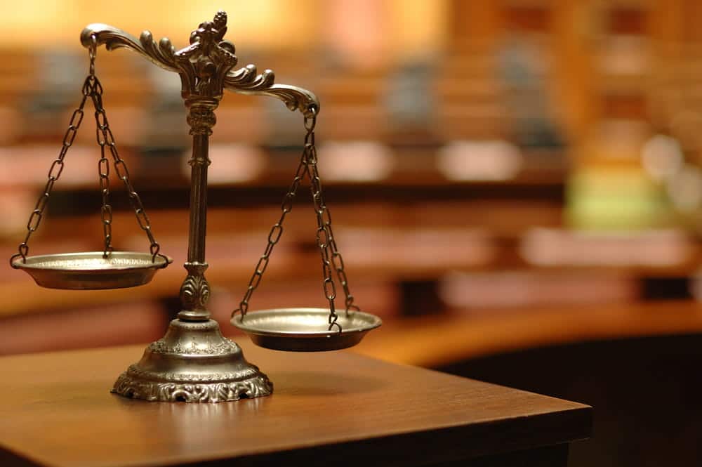 Image is of silver scales of justice sitting on a wooden table in a courtroom, concept of a domestic violence case
