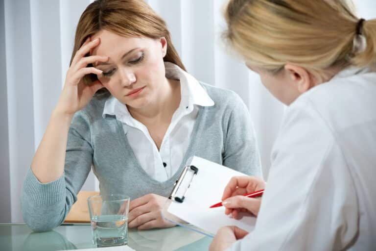 Image is of a woman speaking with a therapist who is taking notes during a counseling session, concept of domestic violence and mental health assessment and guidance.