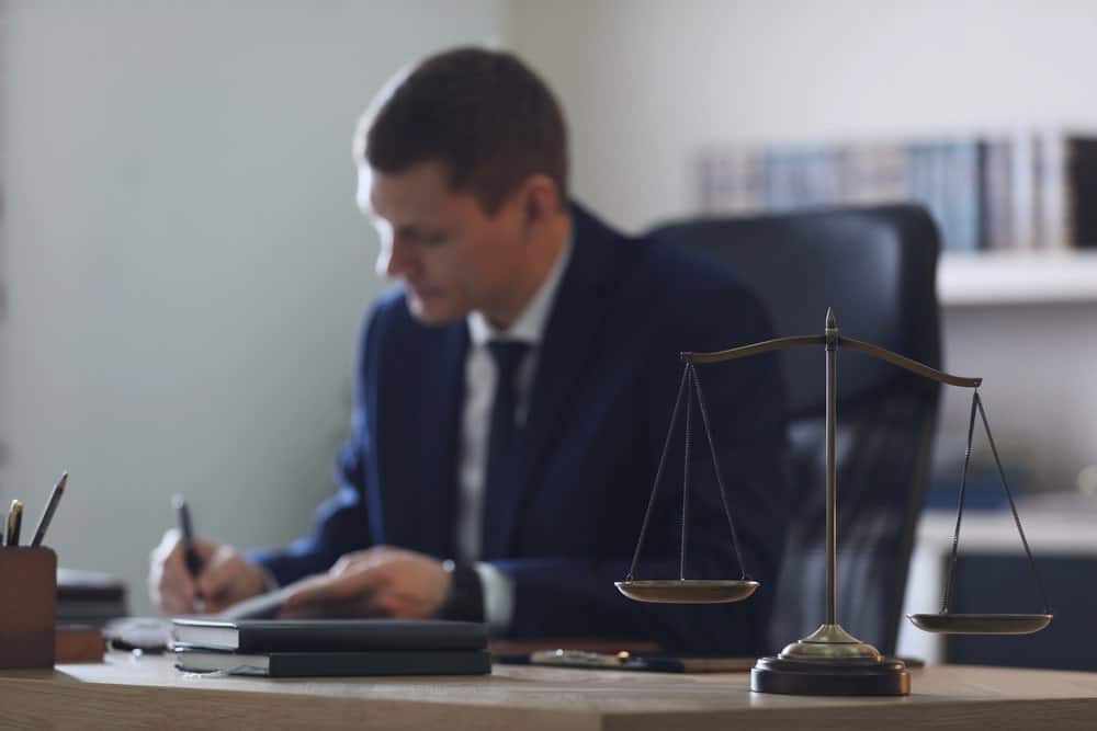 Image is of a lawyer writing notes at a desk with scales of justice in front, concept of DUI arraignment preparation and legal review