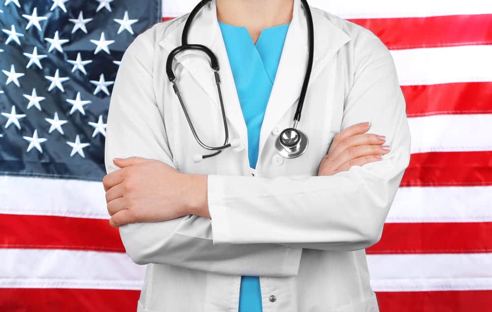 Image is of a medical professional wearing a lab coat with a stethoscope in front of a US flag, representing licensing standards and the impact of a DUI in Cocoa Beach on professional credentials