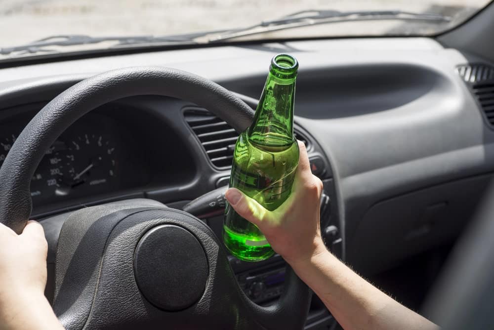 Image is of a driver holding a beer bottle while driving, illustrating the danger of DUI in Cocoa Beach and how it can affect a professional license