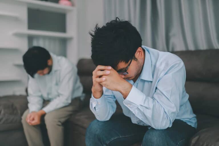 Image is of two men sitting apart in distress after a conflict, concept of domestic violence in same sex relationships