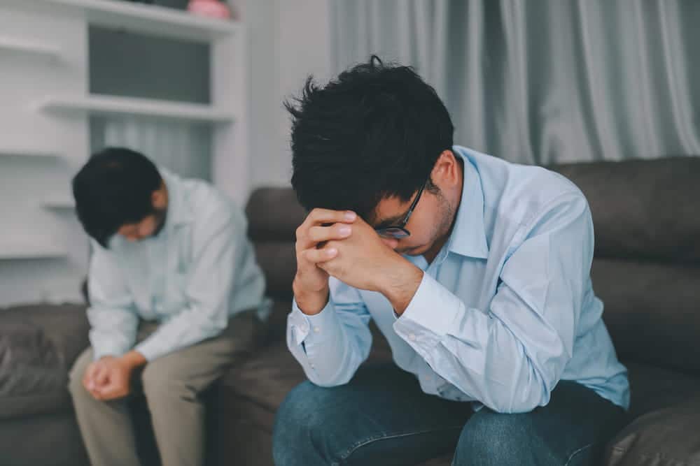 Image is of two men sitting apart in distress after a conflict, concept of domestic violence in same sex relationships