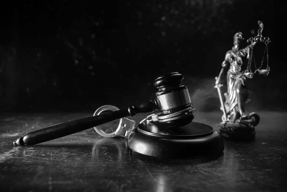 Image is of a gavel, handcuffs, and a justice statue, concept of aggravated domestic violence charges and criminal court proceedings.