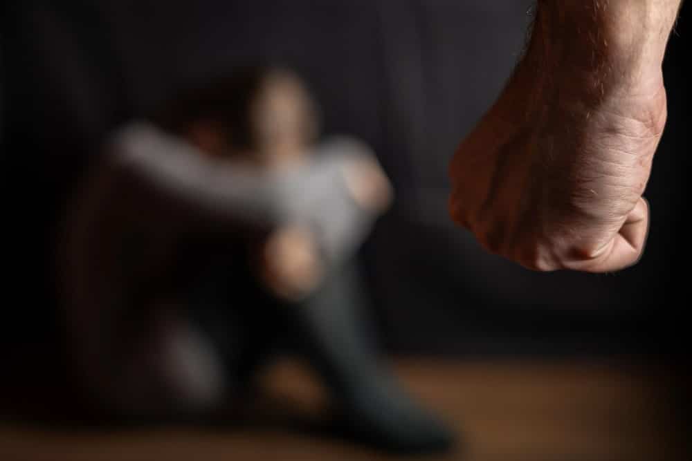 Image is of a woman shielding herself from a threatening raised fist, concept of aggravated domestic violence and fear of physical harm.