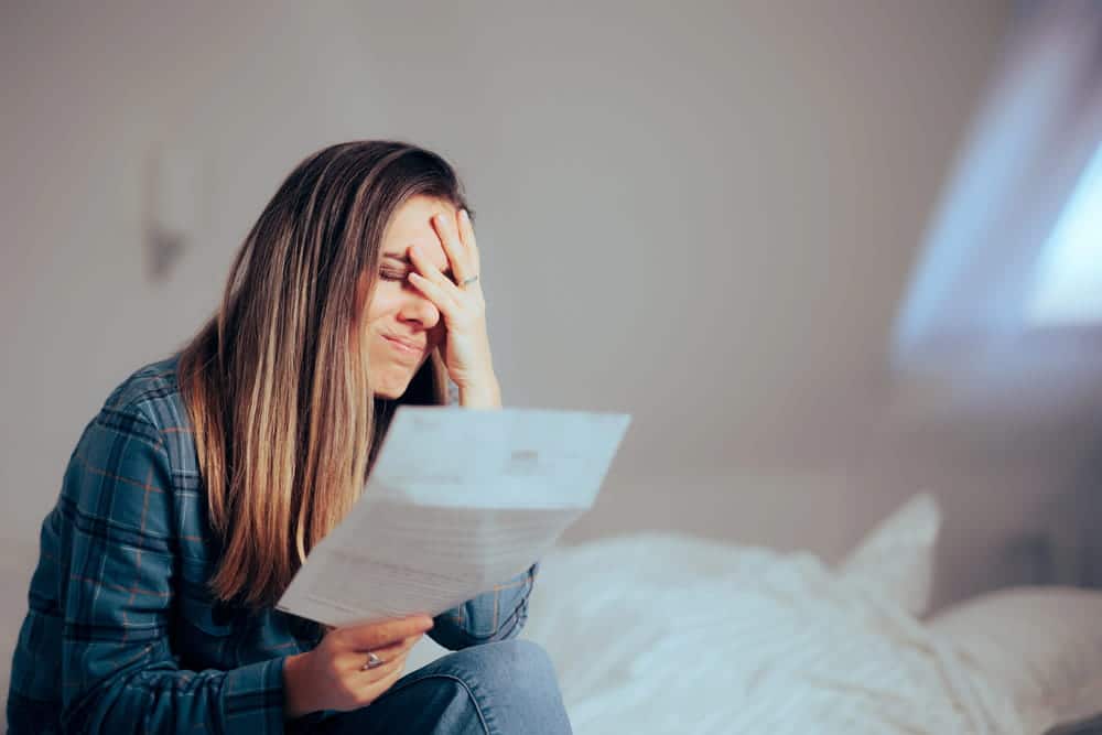 Image is of a woman reading financial documents with a distressed expression, concept of domestic violence in Cocoa Beach and the warning signs of financial abuse.