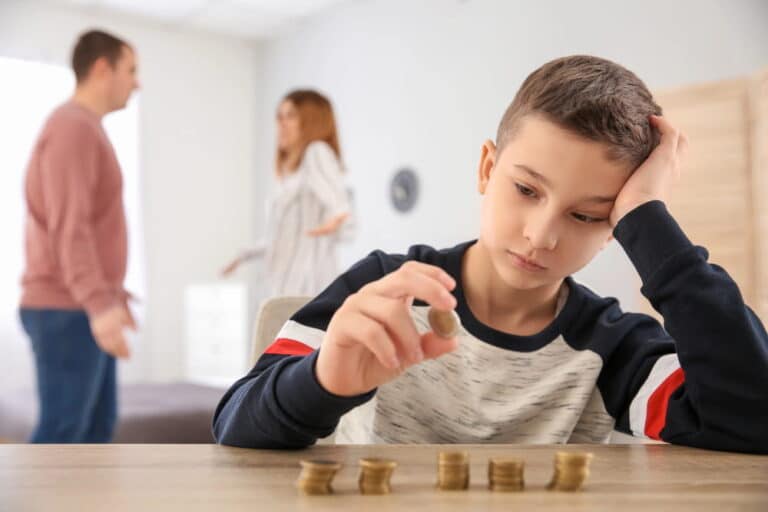 Image is of a child counting coins while parents argue in the background, concept of financial concerns involving child support in Cocoa Beach after domestic violence allegations.