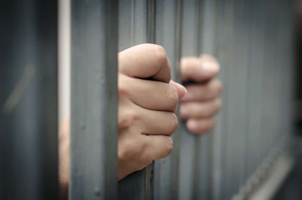 Image is of hands holding jail bars, concept of a Cocoa Beach DUI case involving possible jail time.