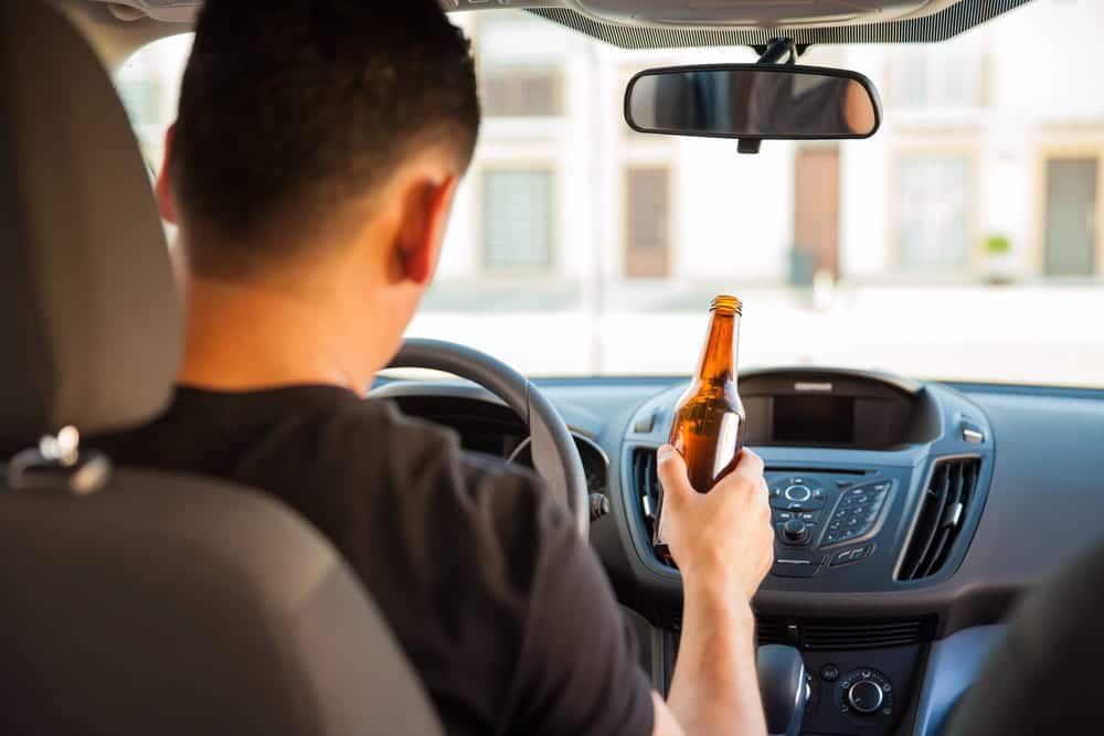 Image is of a driver holding an alcohol bottle inside a vehicle, concept of DUI and reckless driving in Cocoa Beach
