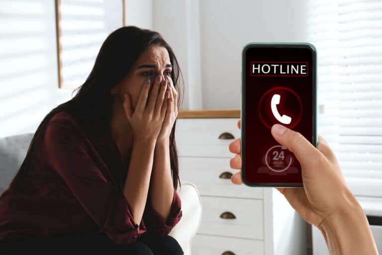 Image is of a distressed woman beside a phone displaying a hotline call, concept of a domestic violence victim seeking help.